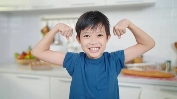 Azjatycki Chłopczyk Niebieskiej Koszuli Demonstrujący Swoje Mięśnie Lub Bicepsy Kuchni — Zdjęcie stockowe