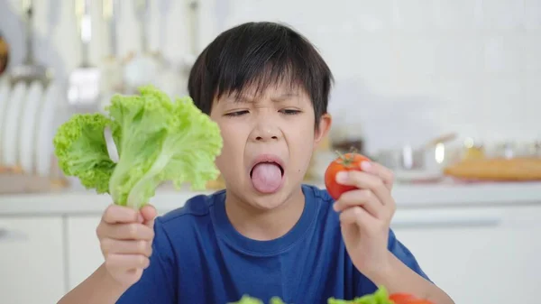 Nutrition and healthy eating habits for kids concept. Asian little boy looking with disgust on vegetable, refusing to eat