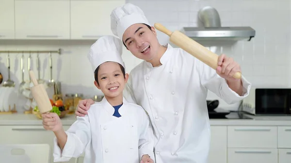 身穿制服的亚洲小男孩和大厨拿着木制滚动销微笑着看着厨房的相机 烹调概念 — 图库照片