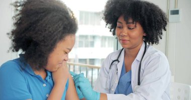 Afro-Amerikalı çocuklar klinikte ya da hastanede aşı oluyorlar ve el hemşiresi koruma için aşı enjekte ediyor. Çocuk aşısı kavramı