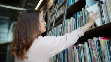 Gözlüklü Asyalı kadın kütüphanede kitap seçiyor.