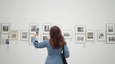 Akıllı telefon kamerasıyla resim çeken genç bir kadın galeride resim çekiyor.