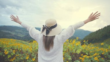 Arkaya bakan kadın kollarını havaya kaldırır sarı çiçek tarlasında ve gün batımında parlak gökyüzünde.