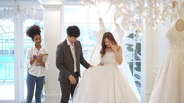新郎はスーツを着て アジアの美しい花嫁は ウェディングスタジオでの結婚式のためのウェディングドレスの選択とフィッティング — ストック写真