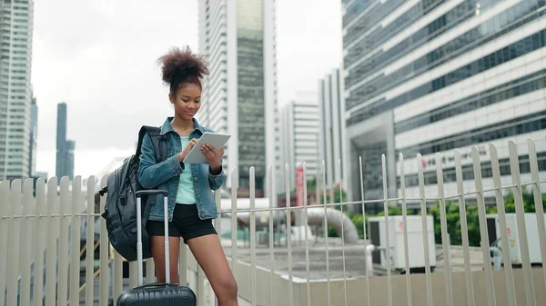 タブレットを使用して市内中心部に立つ若いアフリカ系アメリカ人女性観光客と現代的な高層ビルの背景と笑顔 — ストック写真