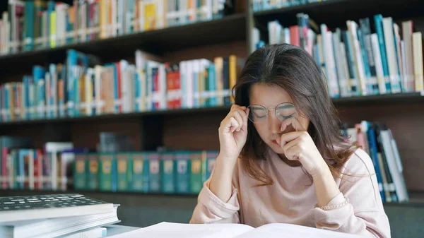 Asian woman student wearing reading glasses for homework and exam preparation in university library and feel pain in the eyes