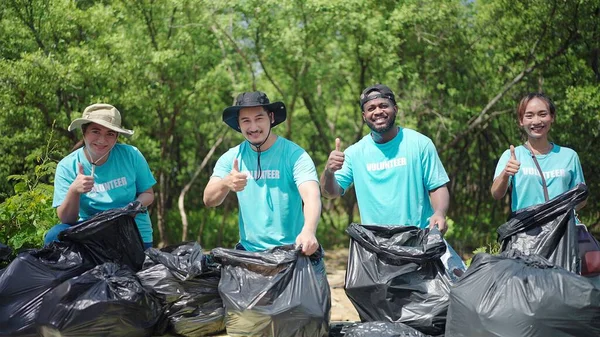 ゴミ袋を持ってカメラを見ている多人種の男性と女性のボランティア 緑の森の中で清掃ボランティア Csr活動 企業の社会的責任 環境問題 — ストック写真