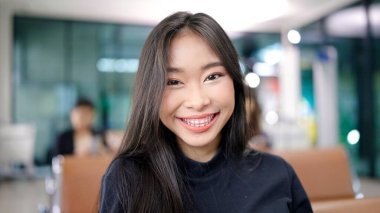 Havaalanı terminalinde uçuşunu beklerken kameraya bakan çekici Asyalı kadın gezgin gülümsemesi. seyahat fikri kavramı