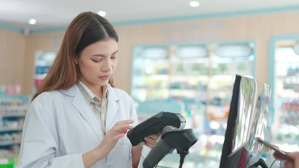 一位年轻的亚洲女药剂师正在使用条形码扫描仪为药店的顾客付款 — 图库照片