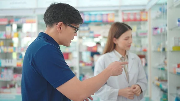 Asian male customers talking with professional woman pharmacist to buy medicine for an illness in a pharmacy