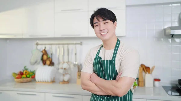 年轻的亚洲人 身穿围裙 微笑着站在家里厨房里 双手交叉 自信地站在那里拍照 — 图库照片