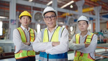 Asyalı mühendislerden oluşan bir portre ekibi güvenlik üniformalı adamlar sanayi fabrikasında kolları çapraz dururken kameraya bakıyor. Takım çalışması konsepti
