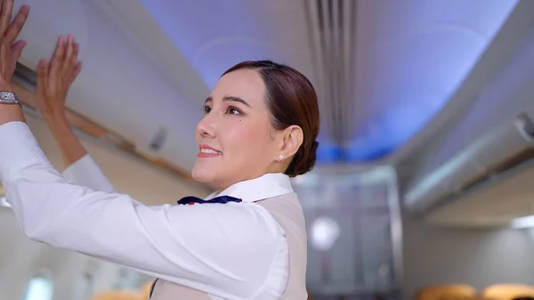 stock image Asian women flight attendant in uniform closing overhead luggage bin in airplane. Checking overhead luggage bin before airplane take off