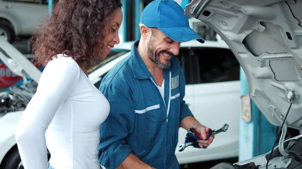 車の修理店で女性の顧客に点検し 維持を説明する均一なオープン車両の自動車整備士 車のサービス メンテナンスの概念 — ストック写真