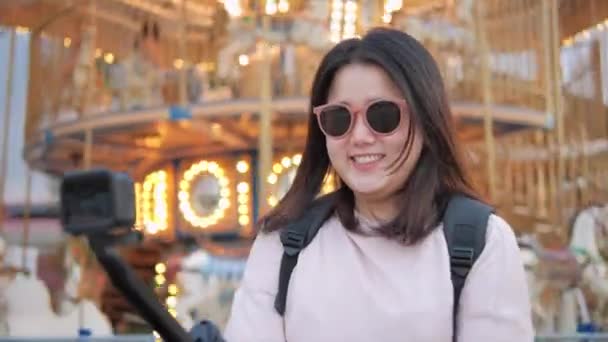 アジアの女性旅行者は 遊園地で休暇の週末の場所を示すために陽気な動きでカメラを持ちます — ストック動画