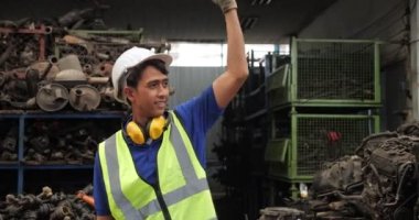 Asyalı işçi üniforma giyer. Mühendisleri selamlar. Forklift araba kullanmak için el işareti yapar..