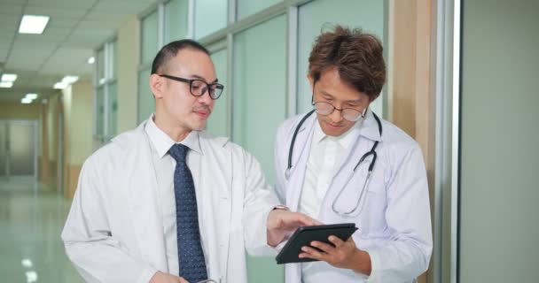 アジアの2人の医師が患者診断データを話し合い 議論する病院の廊下にデジタルタブレットコンピュータ技術を保持します — ストック動画