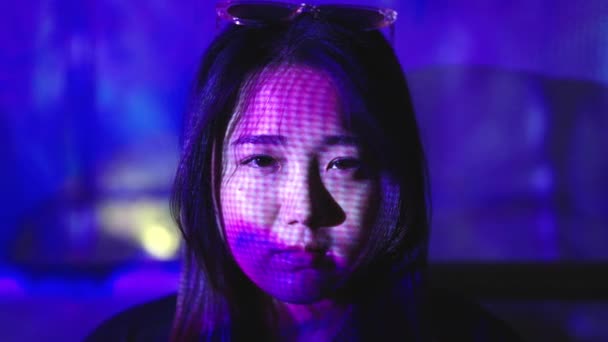 夜間に顔にネオンカラフルなライトでカメラを見て眼鏡をかけている若いアジアの女性の肖像画を閉じます — ストック動画