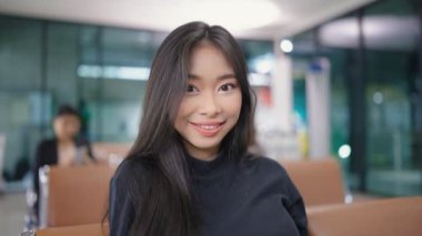 Havaalanı terminalinde uçuşunu beklerken kameraya bakan çekici Asyalı kadın gezgin gülümsemesi. seyahat fikri kavramı