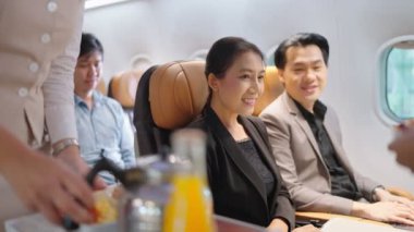 Dost canlısı Asyalı kadın uçuş görevlisi yemek servisi yapıyor ve uçaktaki yolcularla konuşuyor. Havayolu hizmeti
