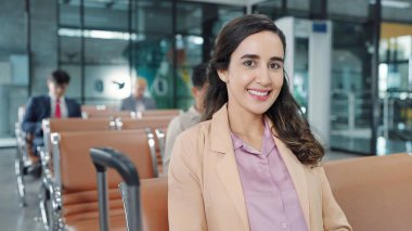 Havaalanının terminal kapısında oturmuş kameraya bakan Latin kökenli genç yolcunun gülümseyen yüzünü kapatın. Seyahat kavramı