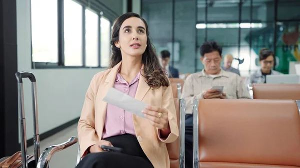 若いヒスパニック系の女性乗客国際空港で待っているターミナル出発ゲートの椅子に座っている間に出発搭乗券をチェック — ストック写真