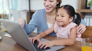Mutlu Asyalı anne ve kız online çalışmak ya da ödev yapmak için dizüstü bilgisayar kullanıyor. Anne kızına dizüstü bilgisayar kullanmasında yardım ediyor. Çevrimiçi eğitim, Teknoloji konsepti