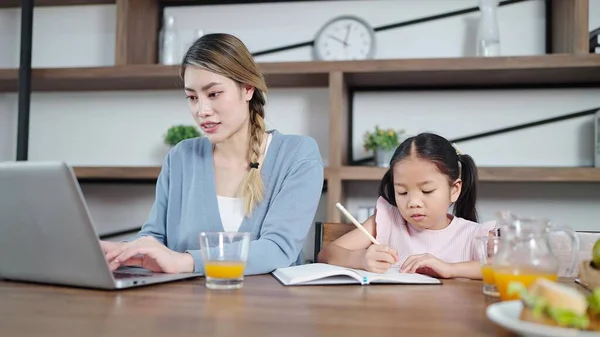 Молода Азіатська Мати Працює Ноутбуці Поки Маленька Дочка Робить Домашнє — стокове фото
