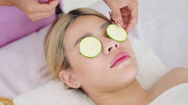 一个漂亮的女人躺在温泉床上 用新鲜的黄瓜片遮住她的眼睛 治疗师在病人的眼睛上涂上新鲜黄瓜片 皮肤护理概念 — 图库照片