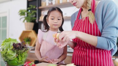 Evdeki mutfak odasında annesinin elmasına bakan Asyalı küçük kızın gülümseyen yüzünü kapat. Sağlık hizmetleri için meyve yiyorum. Mutlu Asyalı aile, sağlıklı gıda konsepti