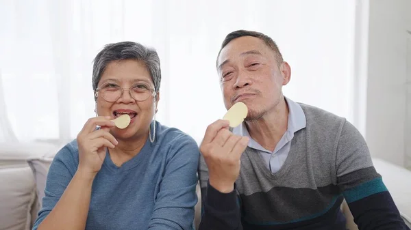 Счастливая Пожилая Азиатская Пара Наслаждается Картофельными Чипсами Сидя Удобном Диване — стоковое фото