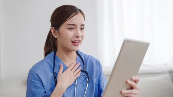 若いアジアの女性医師または看護師は 患者とオンラインでコンサルティングを行っている間 手でタブレットを保持しています 患者とのビデオ会議コールを話す女性看護師 — ストック写真