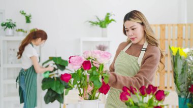 Çiçekçide çalışan önlüklü Asyalı genç bayan çiçekçi. Dükkanda çiçek düzenleyen konsantre genç bayan çiçekçi. Küçük işletme kavramı