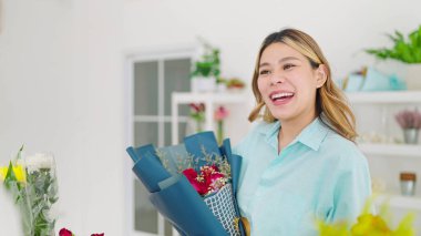 Çiçekçiden bir buket gül almaya gelen mutlu Asyalı kadın müşteri. Çiçekçide elinde gül buketi tutan güzel bir Asyalı kadın.