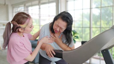 Asyalı yaşlı kadınlar makine üzerinde egzersiz yaparken göğüs ağrısı çekerler. Genç kadınlar egzersiz yaparken göğüs ağrısı çeken annesine bakarlar. Sağlık hizmeti kavramı