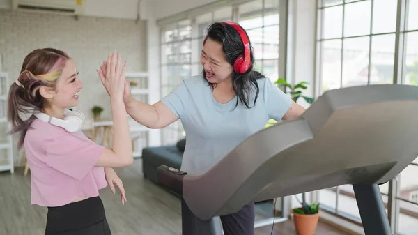 Happy asian elderly women wearing headphones while exercising on treadmill. Elderly women and daughter clapping hands together. Health care concept