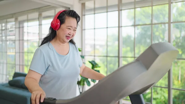 Asian elderly women exercising on the machine in living room at home. Mature woman enjoy doing exercising on treadmill for well being slimming weight. Elderly lifestyle concept