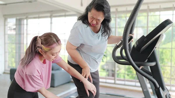 Asian elderly women suffering pain from exercising on the machine and young daughter rushed to take care. Young women take care knee pain of her mother while exercising. Pain from exercise