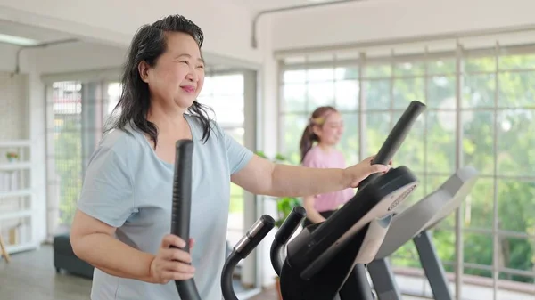 Asian elderly women exercising on the machine in living room at home. Mature woman enjoy doing exercising on treadmill for well being slimming weight. Elderly lifestyle concept