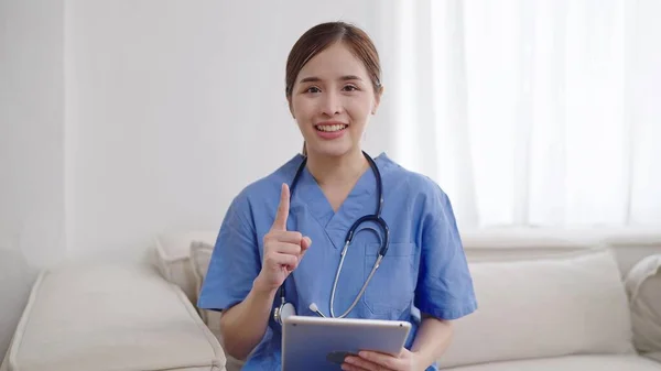 笑着穿制服的年轻的亚洲女医生 用听诊器指着手指向上看相机 亚洲女医生带着第一指尖出现并指出来 同时带着自信的微笑 — 图库照片