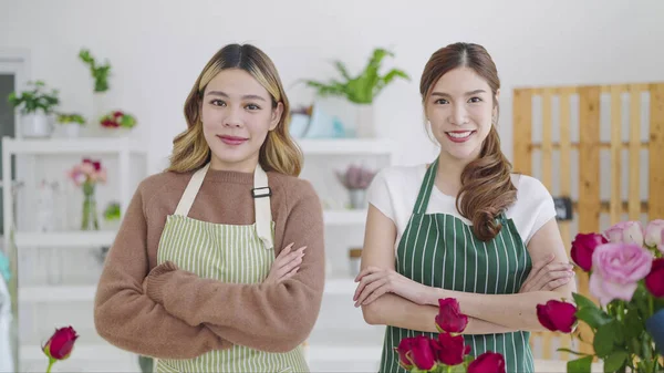 Portrait of two beautiful asian woman florist in apron standing with arms crossed in flower shop and smiling to camera. Two asian woman owned of flower shop. Florist concept, Small business owner