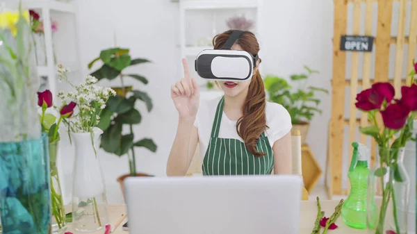 Young asian women owner floral store wearing VR glasses moving hands in air for working and select flowers through virtual reality headset. Business and technology concept, Metaverse virtual