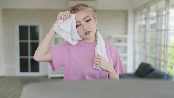 アジアの若い女性は自宅でマシンで運動します 楕円マシンで走っているスポーティな女性 機械で運動しながらあなたの顔に汗を拭くタオルを使用している若い女性 — ストック写真