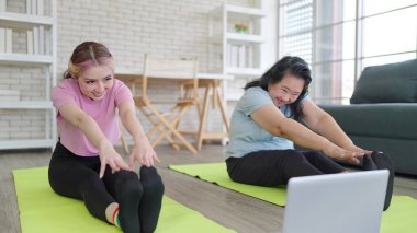 Mutlu genç Asyalı kız ve yaşlı anne dizüstü bilgisayardan video eğitimi izliyorlar. Kız ve yaşlı anne evde birlikte egzersiz yapmaktan hoşlanıyorlar. Aile etkinliği kavramı