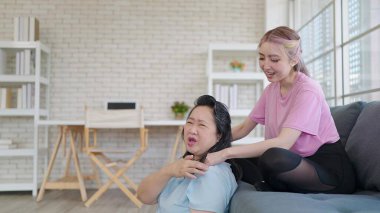 Asyalı kız, evde oturma odasında dinlenirken yaşlı anneye omuz masajı yapıyor. Genç kız yaşlı bir anneye masaj yapıyor. Aile yaşam tarzı