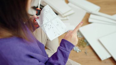 Genç Asyalı kadın vida tutuyor, evde tek başına mobilya montaj rehberini okuyor. Yeni mobilya montajı, mobilya montajı