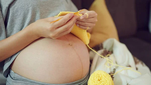 Women pregnant knitting handcraft clothes for her upcoming baby. Close up hands of pregnant woman doing knitting handcraft clothes for baby. Pregnancy concept