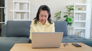 Asyalı orta yaşlı kadınlar evdeki oturma odasında kanepede otururken dizüstü bilgisayar kullanıyorlar. Sosyal medyada çalışan ya da sohbet eden kıdemli kadınlar. Emeklilik yaşam tarzı kavramı