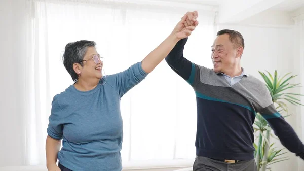 Happy asian senior couple enjoy dancing together in living room at home. Sweet elderly couple enjoy love moment. Retirement lifestyle of asian couple senior concept