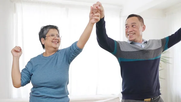Happy asian senior couple enjoy dancing together in living room at home. Sweet elderly couple enjoy love moment. Retirement lifestyle of asian couple senior concept